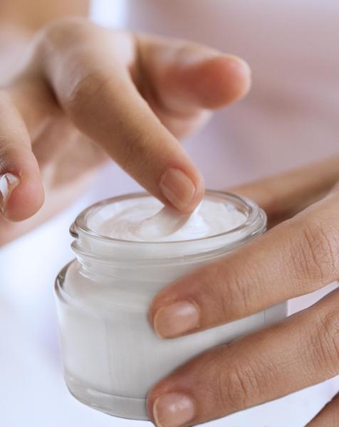 A person using their finger to get lotion out of a jar.